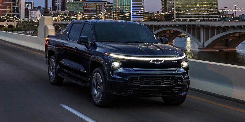 2025 Chevrolet Silverado EV Headlights On with City in Background Belfast, ME