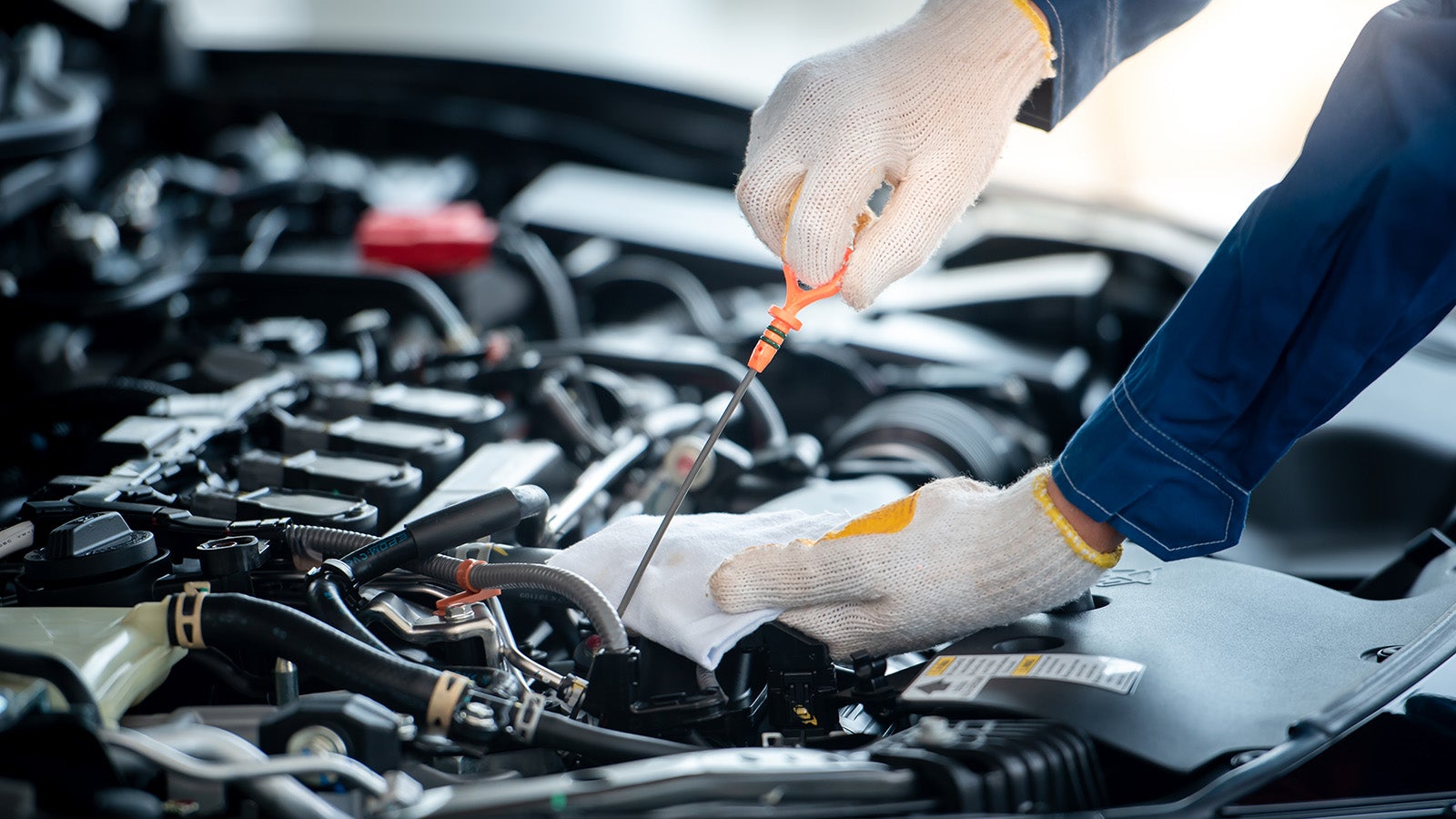 Mechanic checking engine oil with dipstick wearing gloves
